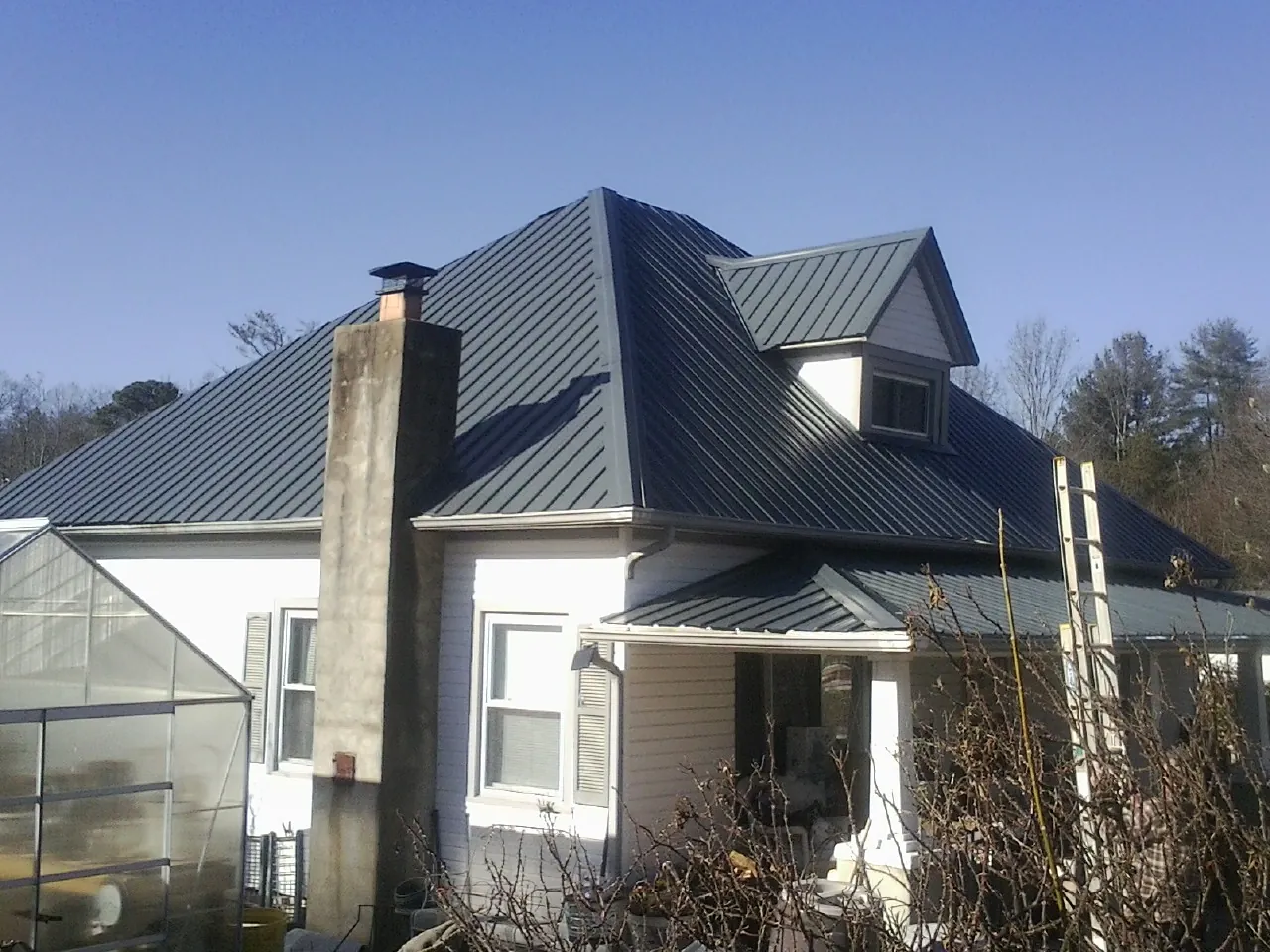 Dark blue standing seam metal roof on a white farmhouse with dormer — Slate & Tile Roof Repair by Roofing Brothers in Newbern