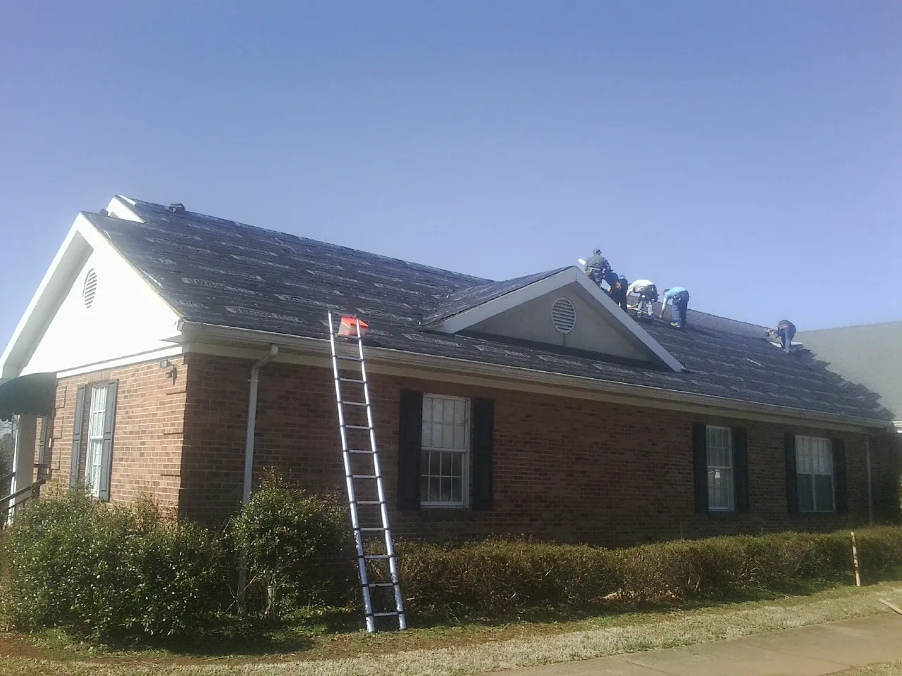 Crew tearing shingles off a brick ranch roof with a ladder set — Emergency Roof Repair work by our crew in Newbern