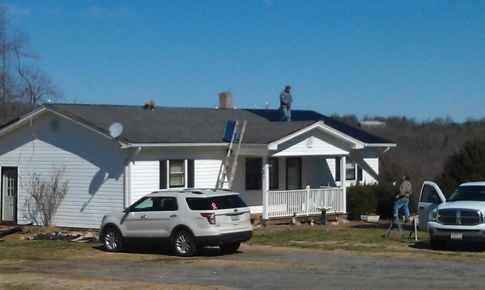 Roofers stripping shingles from a white ranch house roof in Newbern