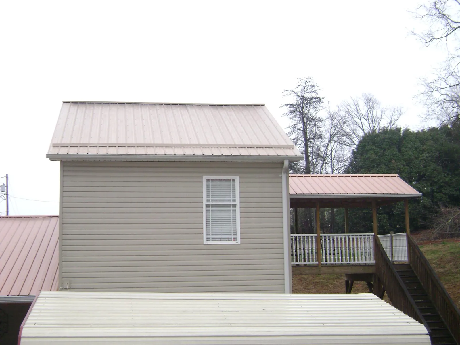 Tan metal roofs on a two story addition and attached porch, from a Roof Replacement job in Newbern